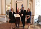 Dr. Magdalena Helmig zeigt zusammen mit Regierungsvizepräsident Florian Luderschmid und offiziellen Repräsentanten Bundesverdienstkreuz mit zugehöriger Urkunde